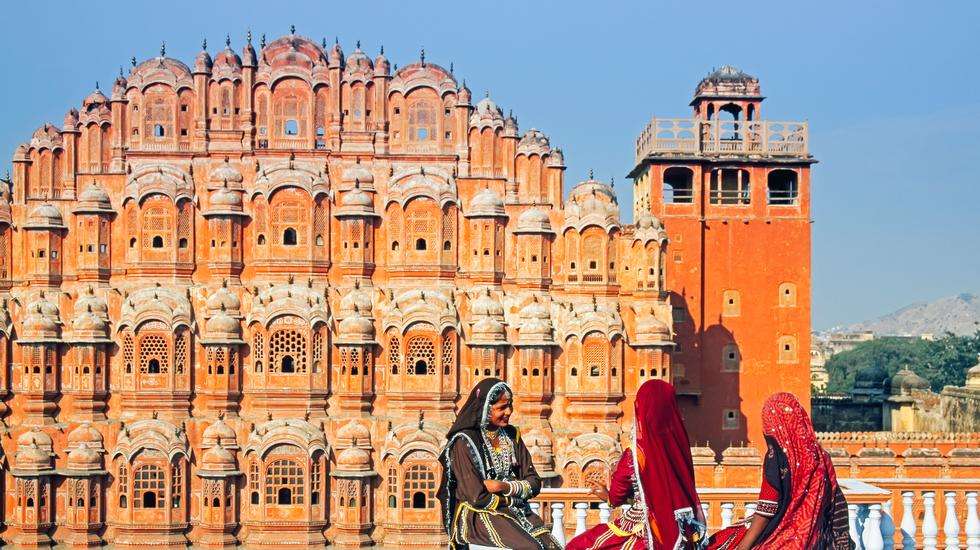 "Three Rajasthani women chatting on a rooftop with the Hawa Mahal palace in the background in Jaipur, Rajasthan, India."