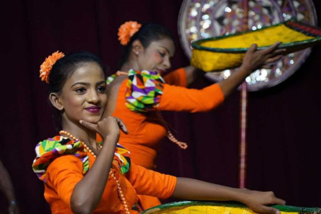 Two women dressed in traditional Sri Lankan outfits dancing on stage.