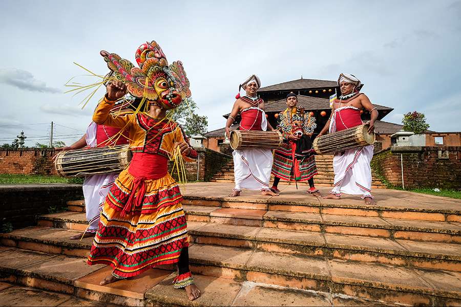 Cultural activity in Sri Lanka featuring men playing dhol and a person wearing a mask of Surpakhha, Ravana's sister, dancing.