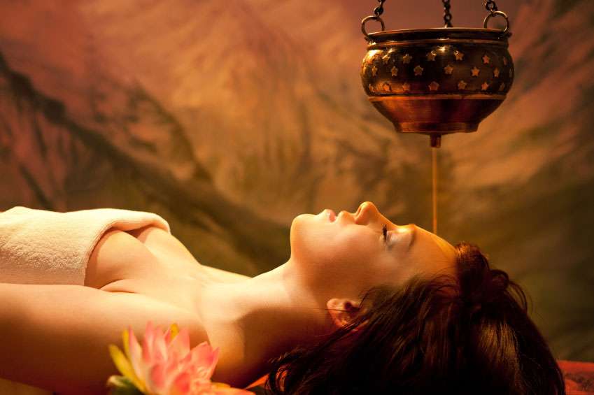 Woman receiving ayurveda treatment in Sri Lanka, with oil being poured on her head while lying down to relax.