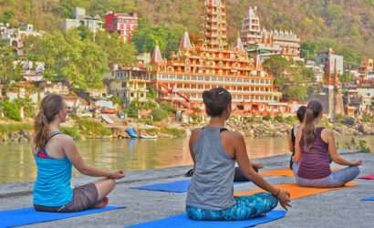 "Girls meditating next to the Rishikesh river with the temple of Rishikesh in the background"