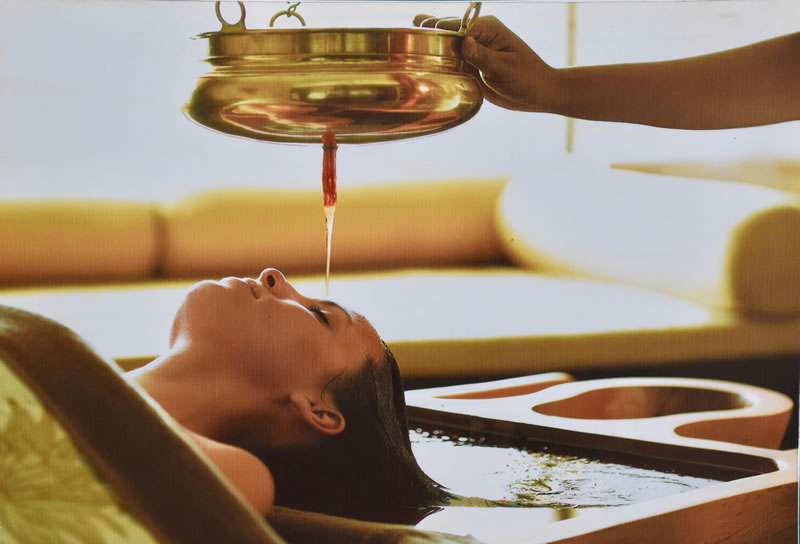 Woman receiving ayurveda treatment in Sri Lanka, with oil being poured on her head while lying down to relax.