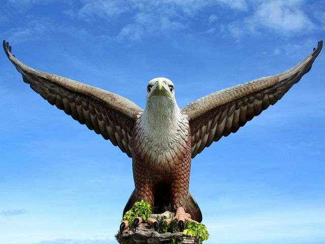 "Dataran Lang eagle statue, a large bronze eagle statue on top of a pedestal against a blue sky background in Langkawi, Malaysia"