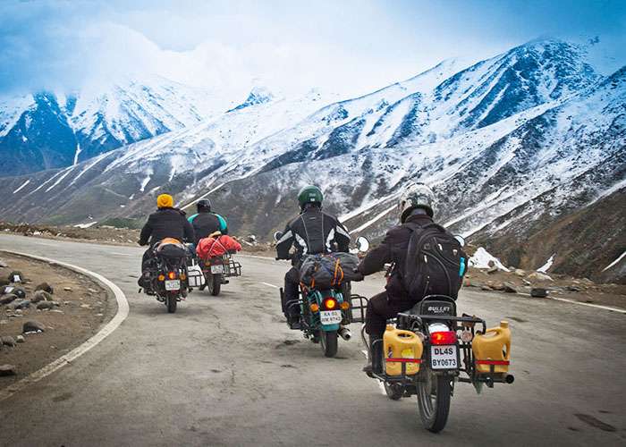 "Tourists riding motorbikes on Ladakh roads with snow-capped mountains in the background"