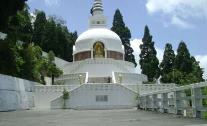 Serene view of the Peace Pagoda in Darjeeling, a gleaming white Buddhist monument amidst lush greenery, offering a peaceful retreat with panoramic views of the Himalayas - a symbol of tranquility and spirituality."