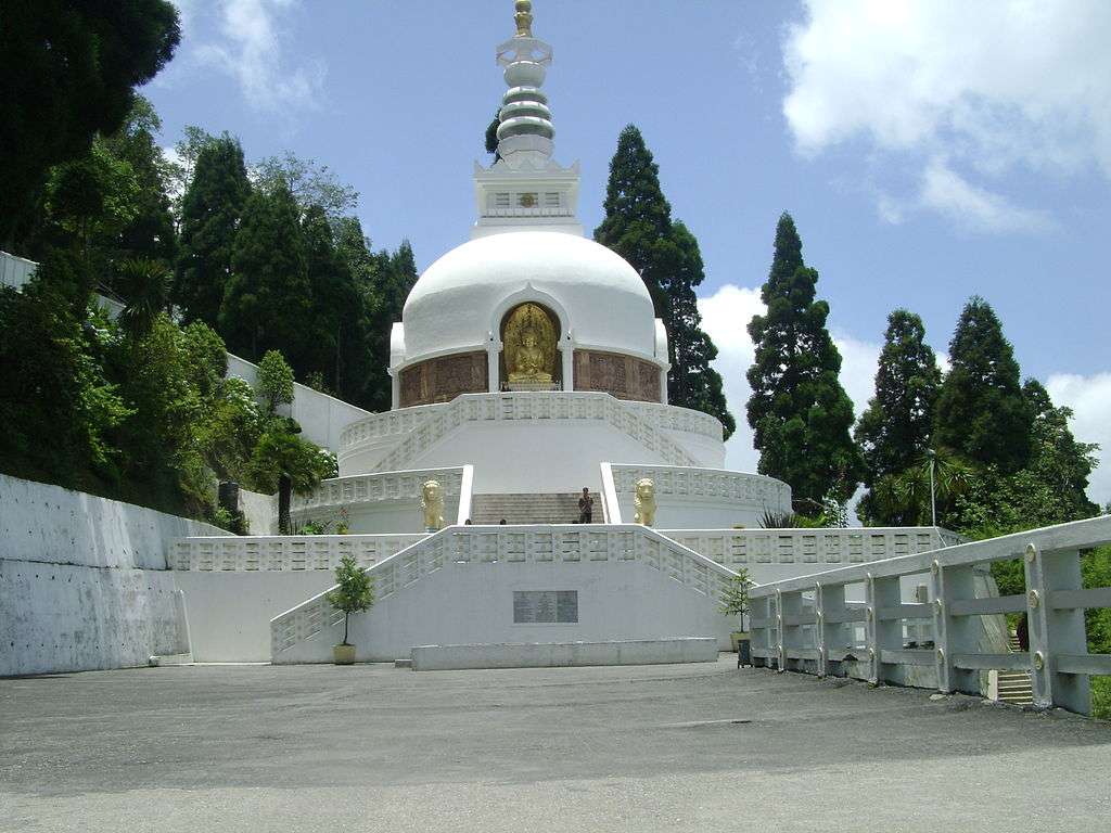 Serene view of the Peace Pagoda in Darjeeling, a gleaming white Buddhist monument amidst lush greenery, offering a peaceful retreat with panoramic views of the Himalayas - a symbol of tranquility and spirituality."