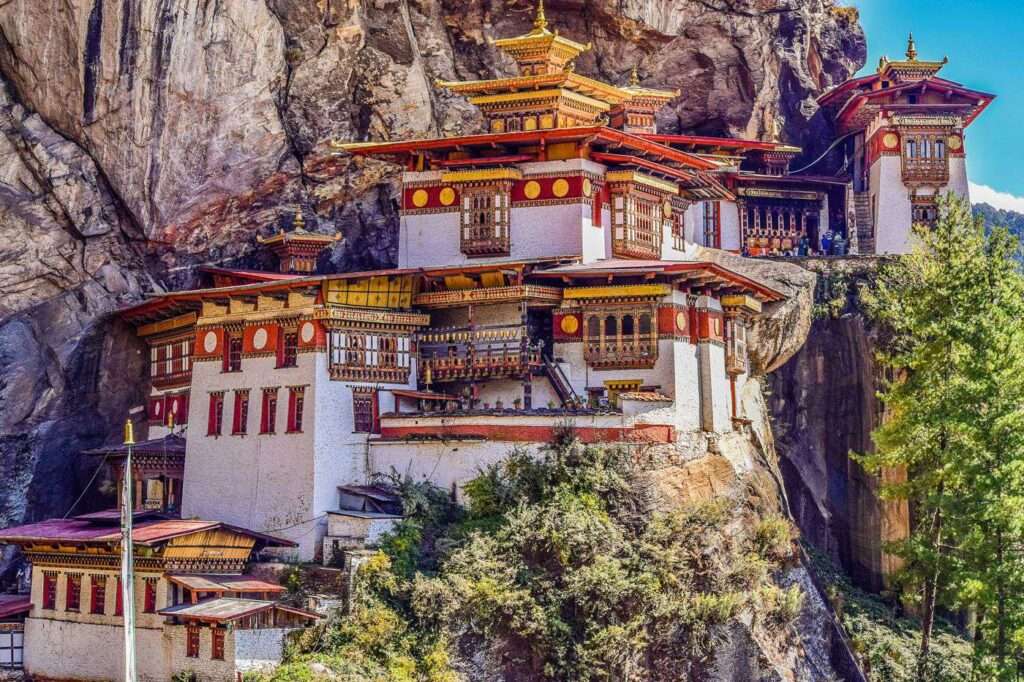 A view of the Tiger's Nest Monastery, a temple complex situated on a cliff in Paro Valley, Bhutan, surrounded by green trees and hills."