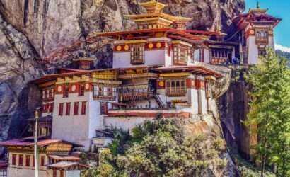 A view of the Tiger's Nest Monastery, a temple complex situated on a cliff in Paro Valley, Bhutan, surrounded by green trees and hills."