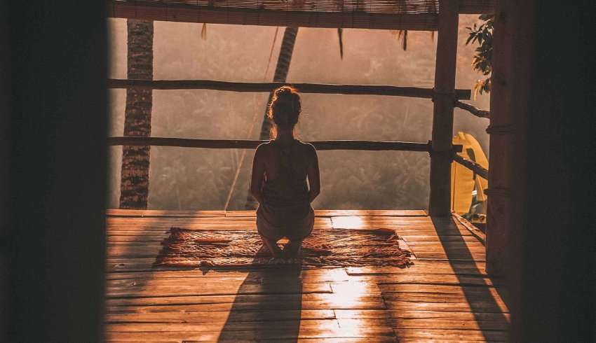 Woman sitting in lotus position with eyes closed meditating in front of ancient temple in Bali.