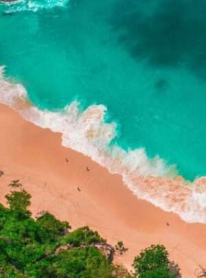 A scenic view of Kelingking beach in Bali, with turquoise blue waters, white sand, and dramatic cliffs in the background.