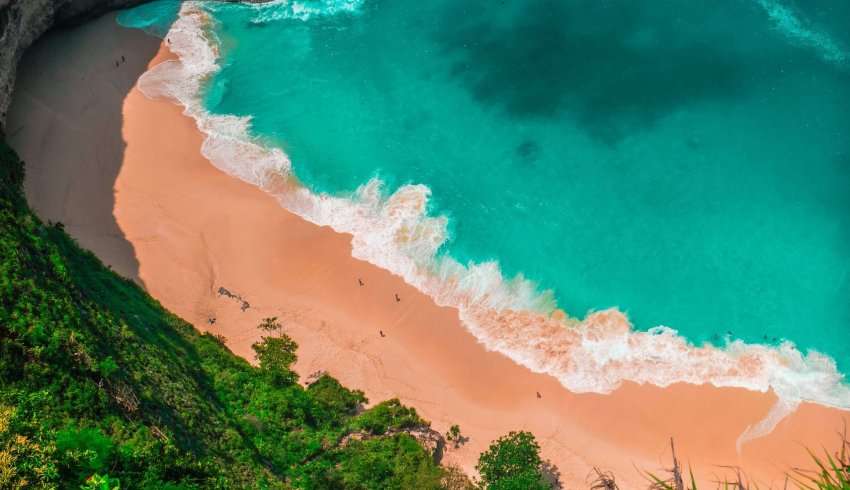 A scenic view of Kelingking beach in Bali, with turquoise blue waters, white sand, and dramatic cliffs in the background.