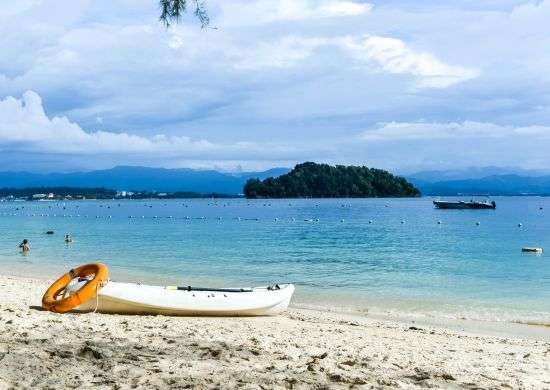 "A person kayaking in turquoise blue waters surrounded by lush green mangrove trees and rocky cliffs in Andaman and Nicobar Islands."