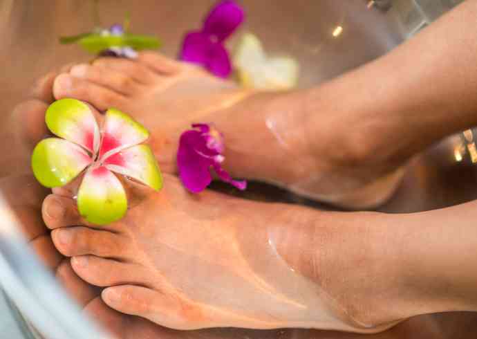 "Close-up of a woman placing her feet in a bowl of flower-infused water at an Ayurveda spa"