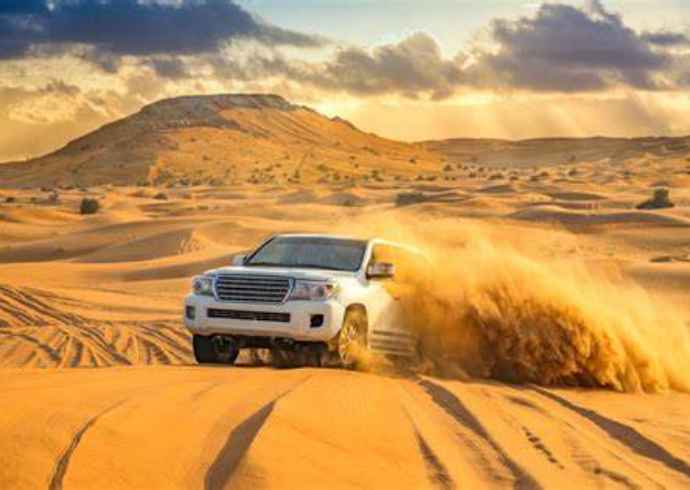 "Off-road vehicle driving through sand dunes in Dubai desert kicking up sand."