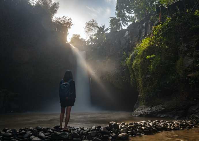 Tourist standing near the waterfall in Tegenungan, Bali, enjoying the natural beauty of the surroundings during an eco-friendly tour.