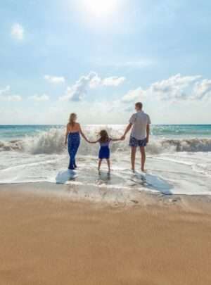 "Family enjoying a beach adventure with parents holding hands of their child"