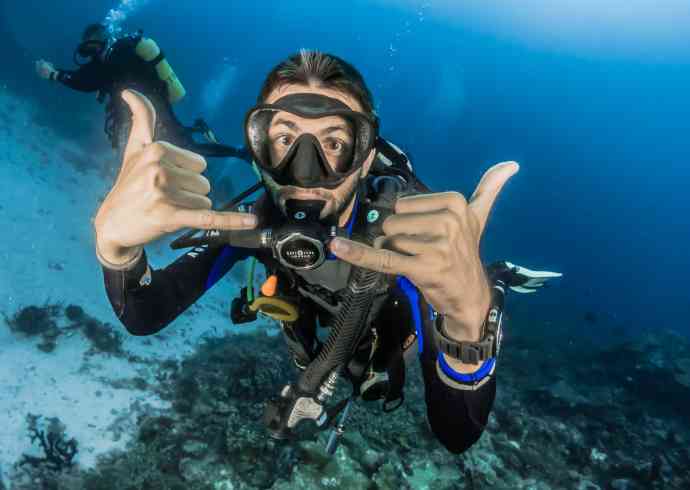 "Two men scuba diving in clear blue water with colorful fish and coral reef in the background"