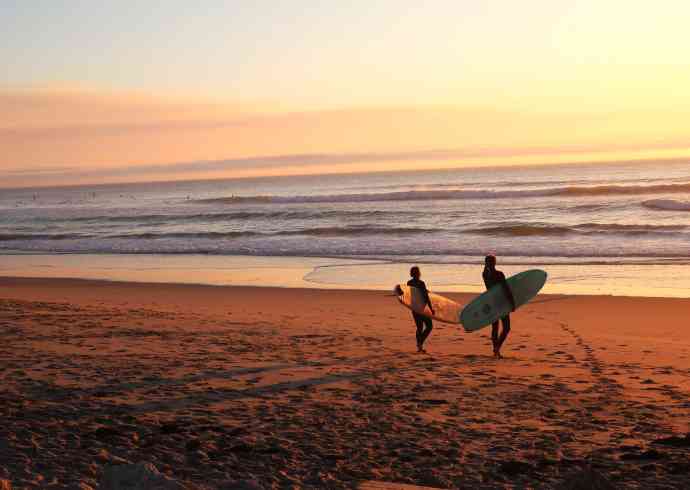 "A couple holding a surfboard, standing on a beach, preparing for a surfing water sport adventure."