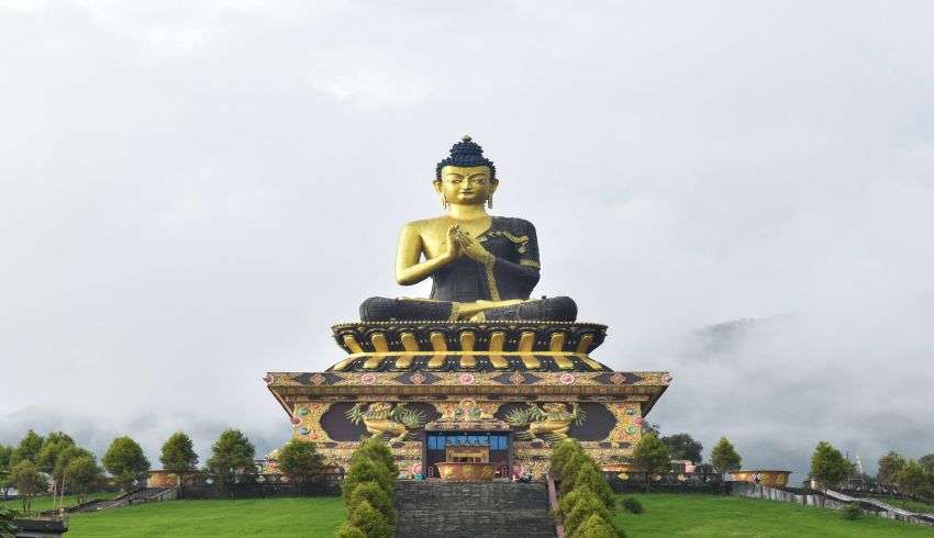 "A giant statue of Buddha in a peaceful garden surrounded by trees and mountains in Ravangla, Sikkim, India."