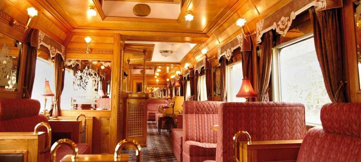 "Interior of Eastern & Oriental Express luxury train compartment with comfortable seats, elegant wooden panels, and a large window overlooking the scenic landscape."