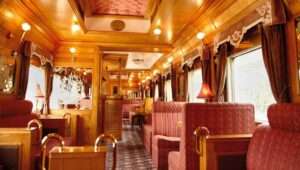 "Interior of Eastern & Oriental Express luxury train compartment with comfortable seats, elegant wooden panels, and a large window overlooking the scenic landscape."