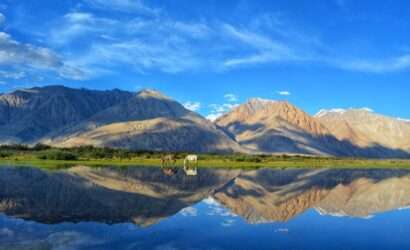 "A stunning view of Tso Moriri Lake surrounded by snow-capped mountains and blue sky"