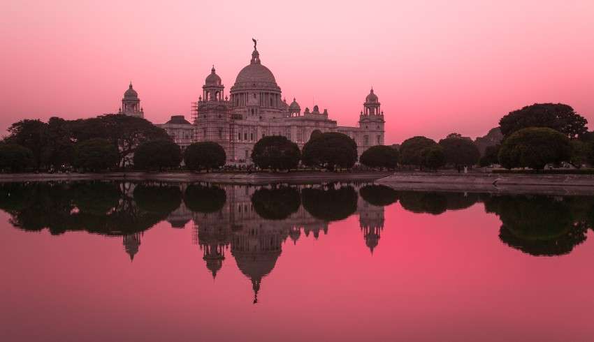 "Victoria Memorial in Kolkata, India, with pinkish hue in the evening light. The white marble building features domes and a central tower with a statue on top."