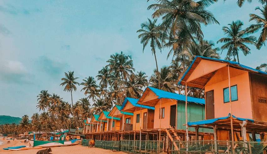 "View of Palolem Beach huts and sea from a raised wooden treehouse with windows overlooking balcony terrace, fishing boats, palm trees and the ocean in South India's Goa region for vacation and holiday."