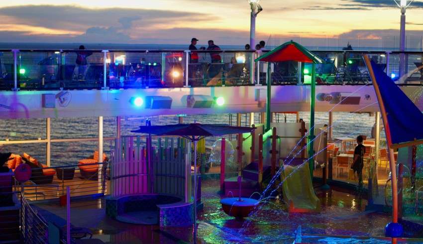 "Passengers having a pool party in the evening on a Royal Caribbean cruise ship. Disco lights are on, and people are sitting, eating, drinking, and having fun."