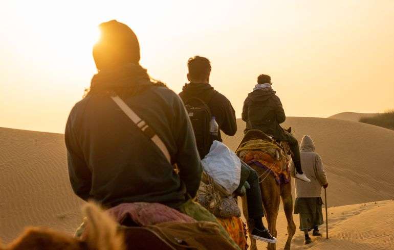 "A tourists riding a camel in the desert landscape of Jaisalmer, India"