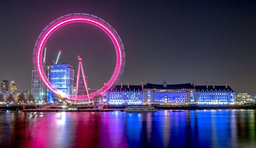 "A pink Ferris wheel illuminating in the night sky in London. "