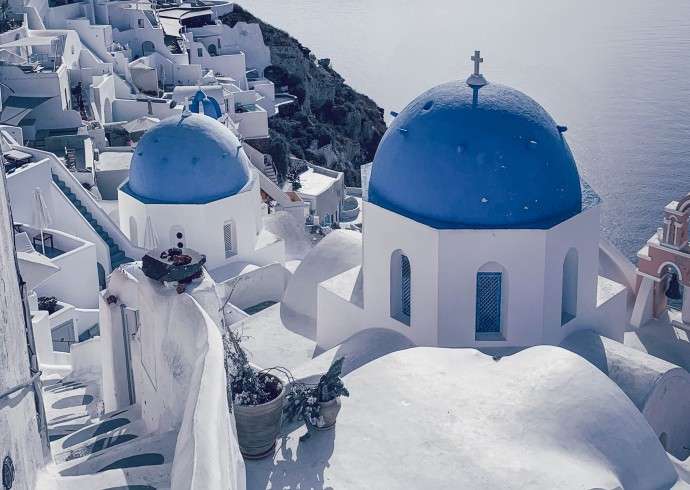 "Blue domes with white buildings in Santorini, Greece against a clear blue sky"