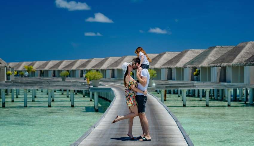 "Honeymoon couple kissing with husband carrying baby on head in Maldives".