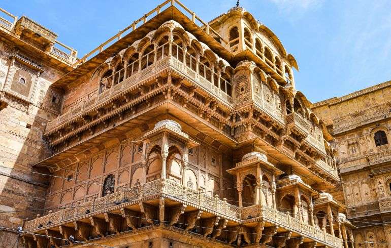 "Jaisalmer Royal Palace in Rajasthan, India - a stunning yellow sandstone palace with intricate architectural details and several towers, overlooking the city."