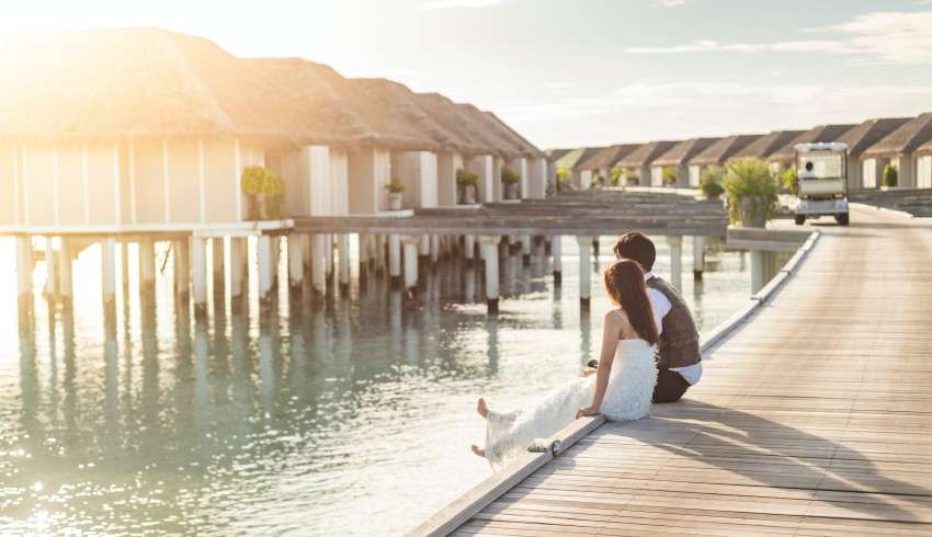 "Honeymoon couple sitting on the corner of the wooden roadway in Maldives, surrounded by turquoise water"