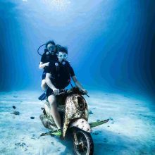 "Suba couple diving in water, sitting on a rusty scooter underwater"